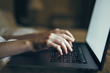 Hands of Caucasian woman typing on laptop in bed