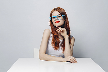 Pensive Caucasian woman sitting at table wearing blue eyeglasses