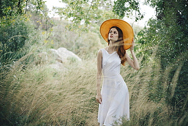 Caucasian woman wearing hat walking in tall grass