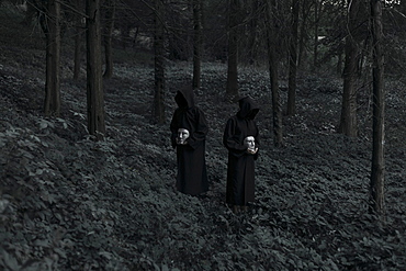 People wearing black robes and holding white masks in forest