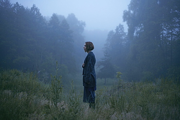 Pensive woman standing in fog in forest