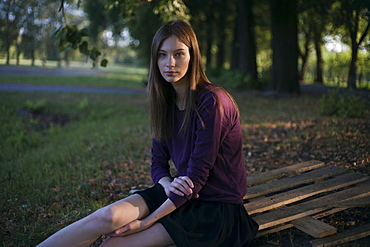 Serious Caucasian woman sitting on wooden pallet in park