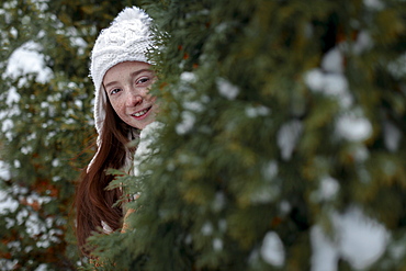 Portrait of Caucasian girl hiding behind tree in winter