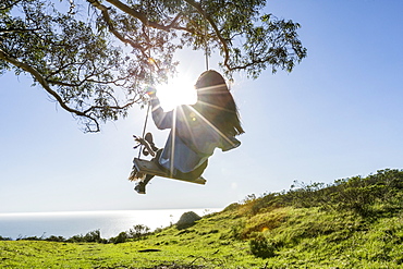 Caucasian woman on tree swing near ocean