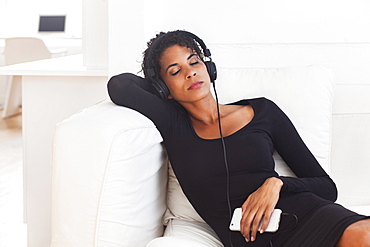 Mixed Race woman on sofa listening to cell phone with headphones