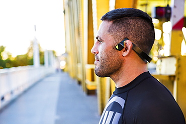 Pensive Caucasian man wearing modern headphones on bridge