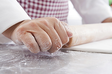 Hands of Hispanic woman using rolling pin on dough