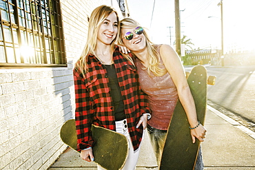 Smiling Caucasian women holding skateboards on sidewalk