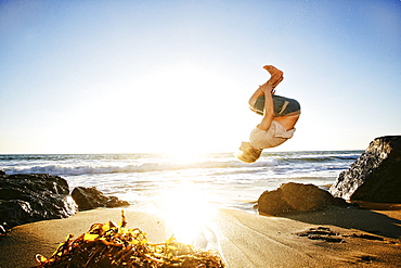 Caucasian man performing backflip on beach