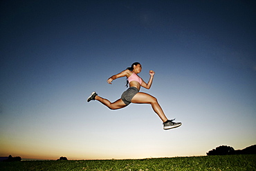 Mixed Race woman running and jumping in field at sunset