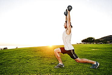 Caucasian man lifting dumbbells in sunny field