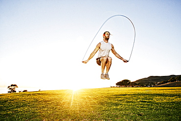 Caucasian man jumping rope in sunny field