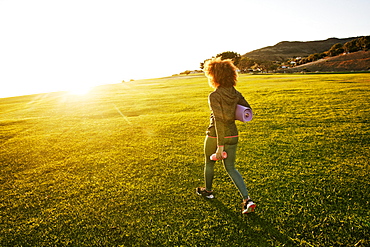 Hispanic woman carrying exercise mat in sunny field