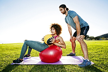 Couple exercising with fitness ball and heavy ball in sunny field