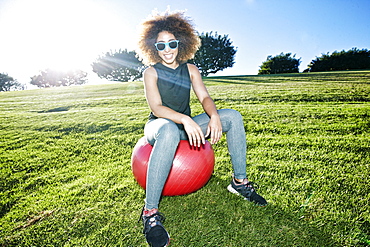 Portrait of smiling Hispanic woman sitting on fitness ball in field