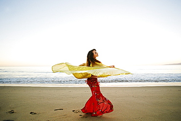 Caucasian belly dancer twirling cape on beach