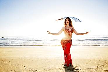 Caucasian belly dancer on beach balancing sword on head