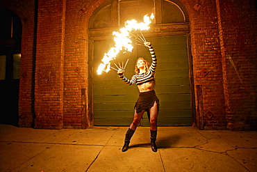 Caucasian woman juggling fire on city sidewalk at night