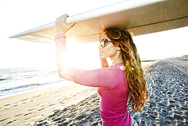 Caucasian woman carrying surfboard on beach