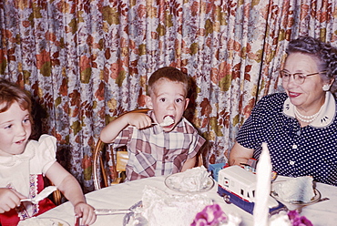 Caucasian woman watching grandson and granddaughter eating cake