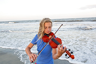 Caucasian girl playing violin at beach