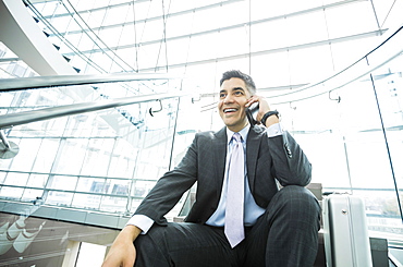 Smiling Mixed Race businessman sitting on staircase talking on cell phone