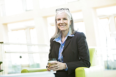 Smiling Caucasian businesswoman sitting in armchair drinking coffee