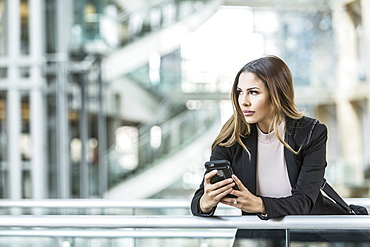 Mixed Race businesswoman texting on cell phone leaning on railing in lobby