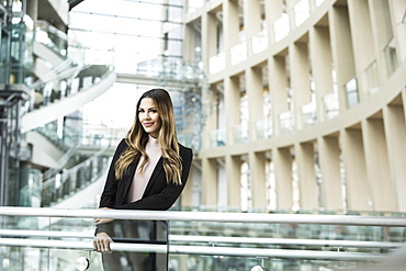 Smiling Mixed Race businesswoman leaning on railing in lobby