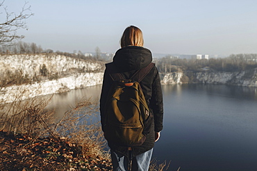 Caucasian woman standing at the edge of reservoir wearing backpack