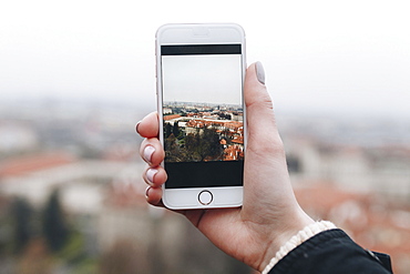 Hand of Caucasian woman photographing cityscape with cell phone