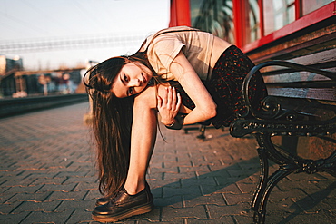 Caucasian woman sitting on bench holding legs