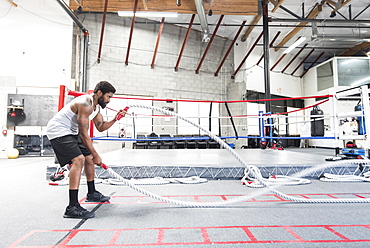 Black man lifting heavy ropes in gymnasium