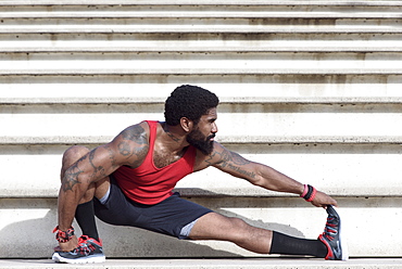 African American man stretching leg on bleachers