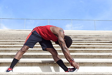 African American man stretching leg on bleachers