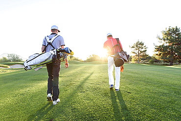 Men carrying golf bags on sunny golf course