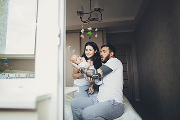 Caucasian mother and father on bed playing with baby son