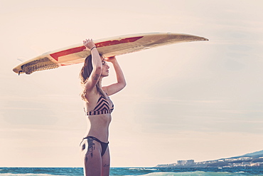 Caucasian woman standing on beach holding surfboard