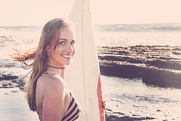 Caucasian woman standing on beach holding surfboard