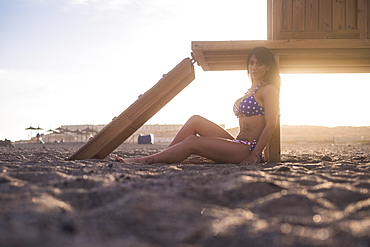 Caucasian woman sitting on beach leaning on cabana