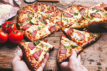 Hands pulling slices of heart-shaped pizza near ingredients on cutting board