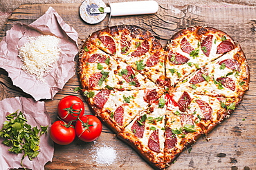 Heart-shaped pizza and ingredients on cutting board