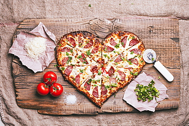 Heart-shaped pizza and ingredients on cutting board