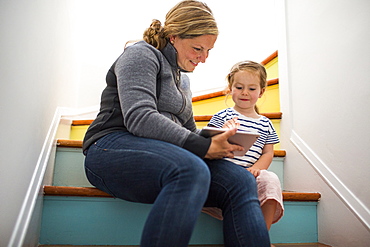 Caucasian mother and daughter using digital tablet on staircase