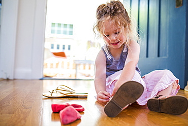 Caucasian girl sitting on floor fastening sandal