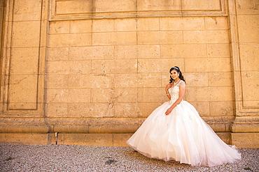 Smiling Hispanic girl wearing gown near wall