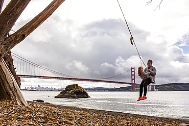 Caucasian mother and daughter on rope spring near bridge