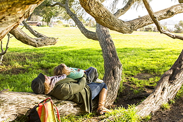 Caucasian mother and daughter laying on tree branch