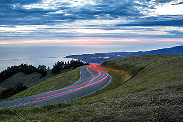 Light trails on winding road near ocean