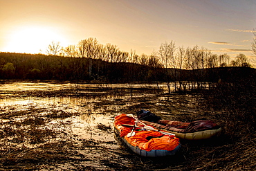 Inflatable rafts on shore of river at sunset